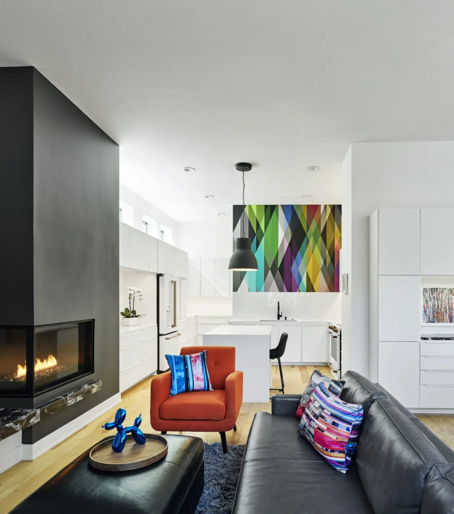 Open living space with modern fireplace, leather sofa, and a kitchen with a colorful geometric backsplash panel.