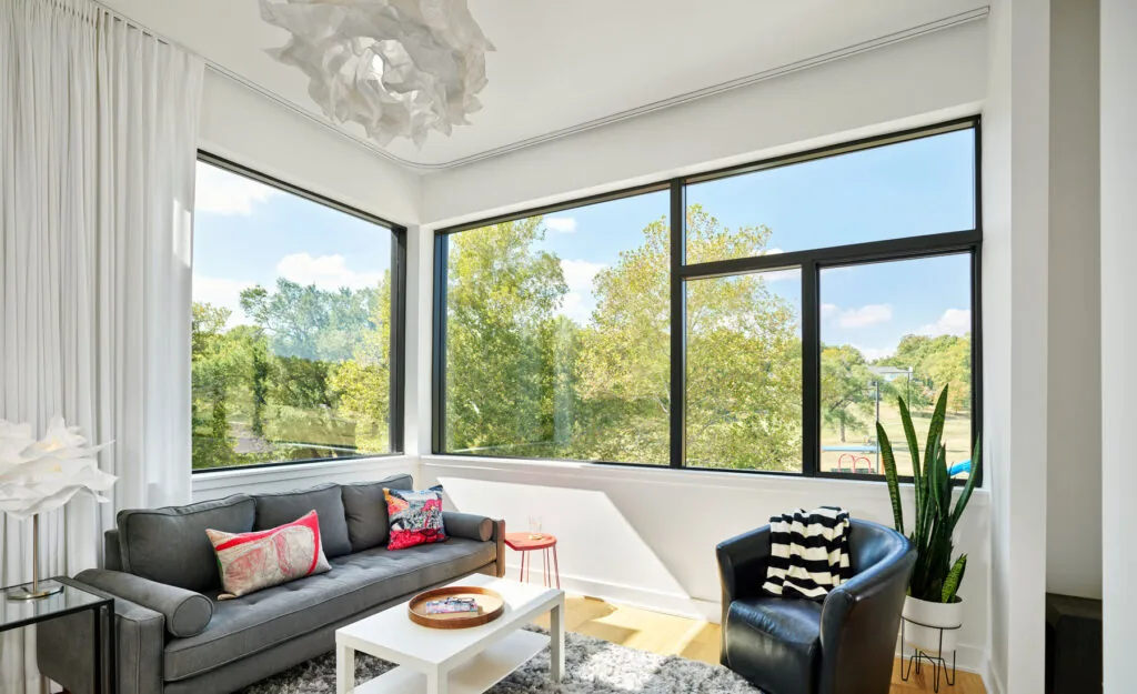 Corner living room at West Plaza Residence features corner windows with black frames overlooking a green landscape.