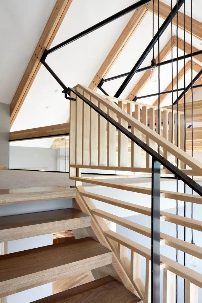 Open staircase with wood treads and railing features black metal supports and exposed wood ceiling beams.