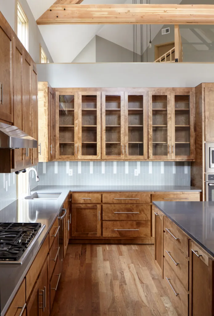 Kitchen in Quackenbush Residence featuring wooden cabinetry, stainless steel counters, and a vaulted ceiling with exposed beams.