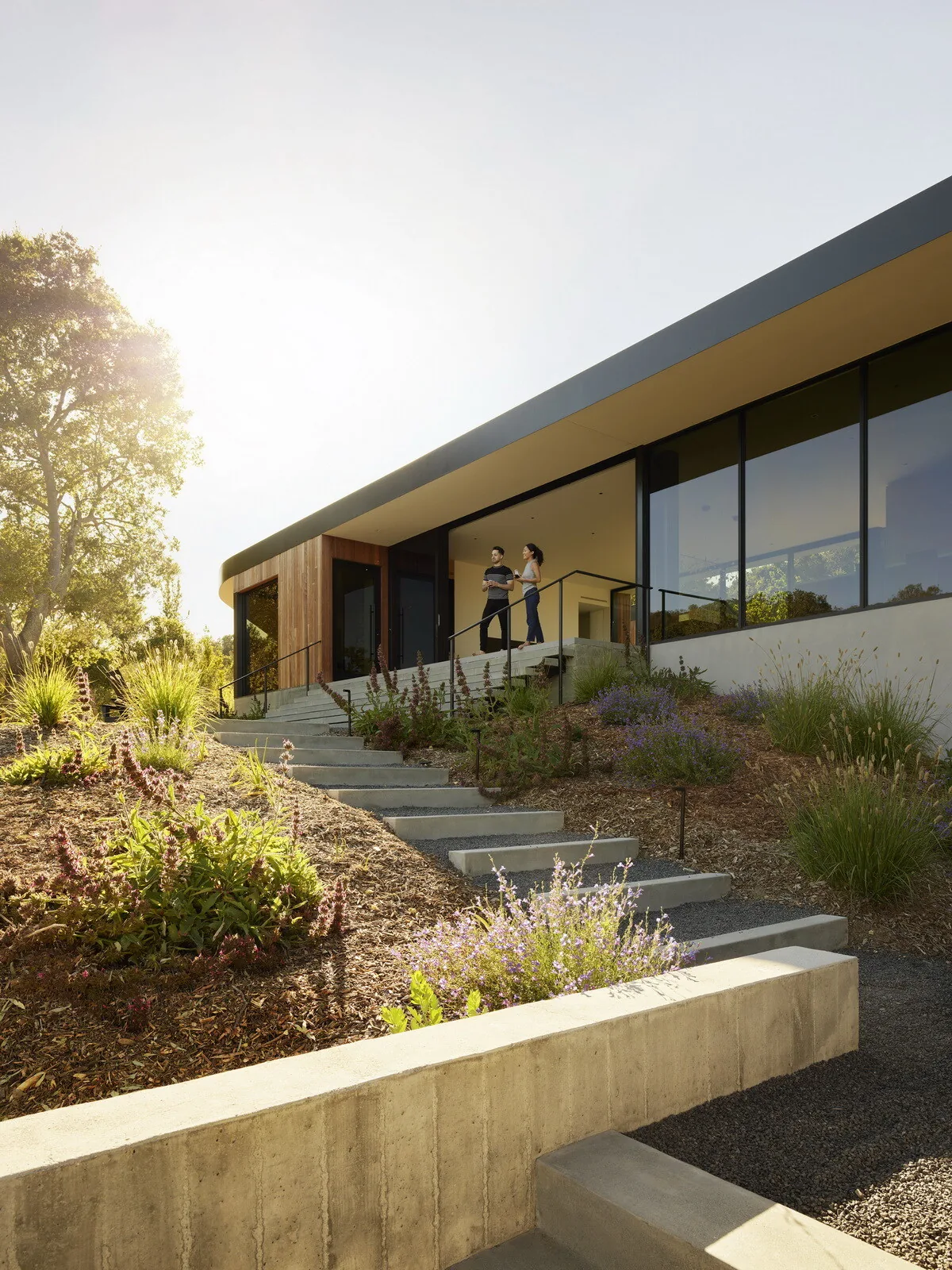 Westridge house features a covered patio with large glass windows and integrated landscaping on a sloped hillside.