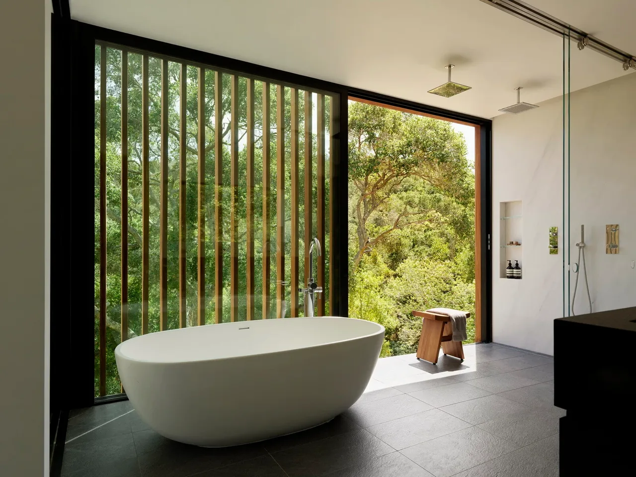 Bathroom featuring a freestanding tub and dual rain shower heads with expansive glass walls revealing outdoor greenery.
