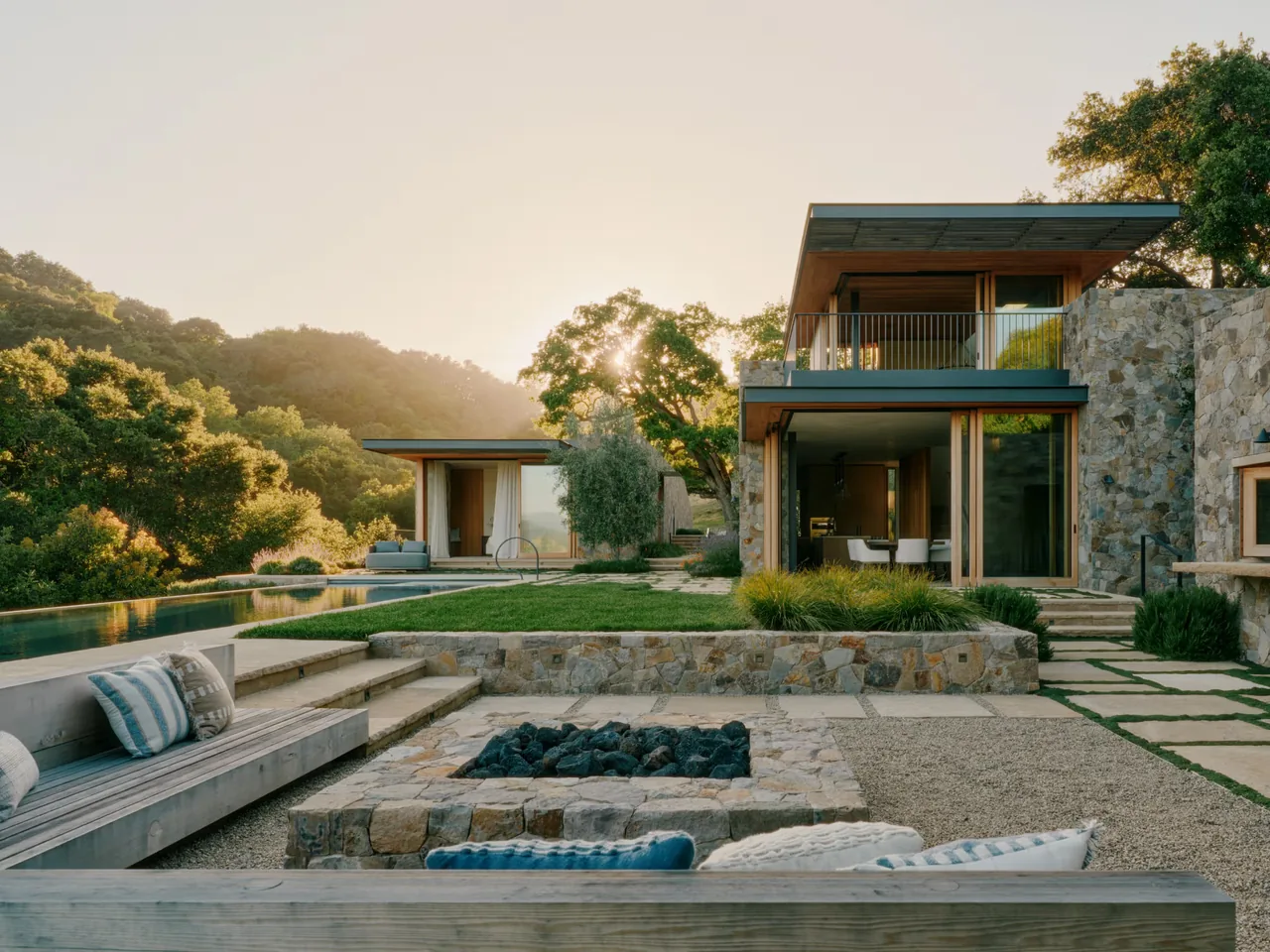 Stone Villa features an outdoor fire pit seating area, natural stone wall cladding, and glass doors opening to the landscape and pool.