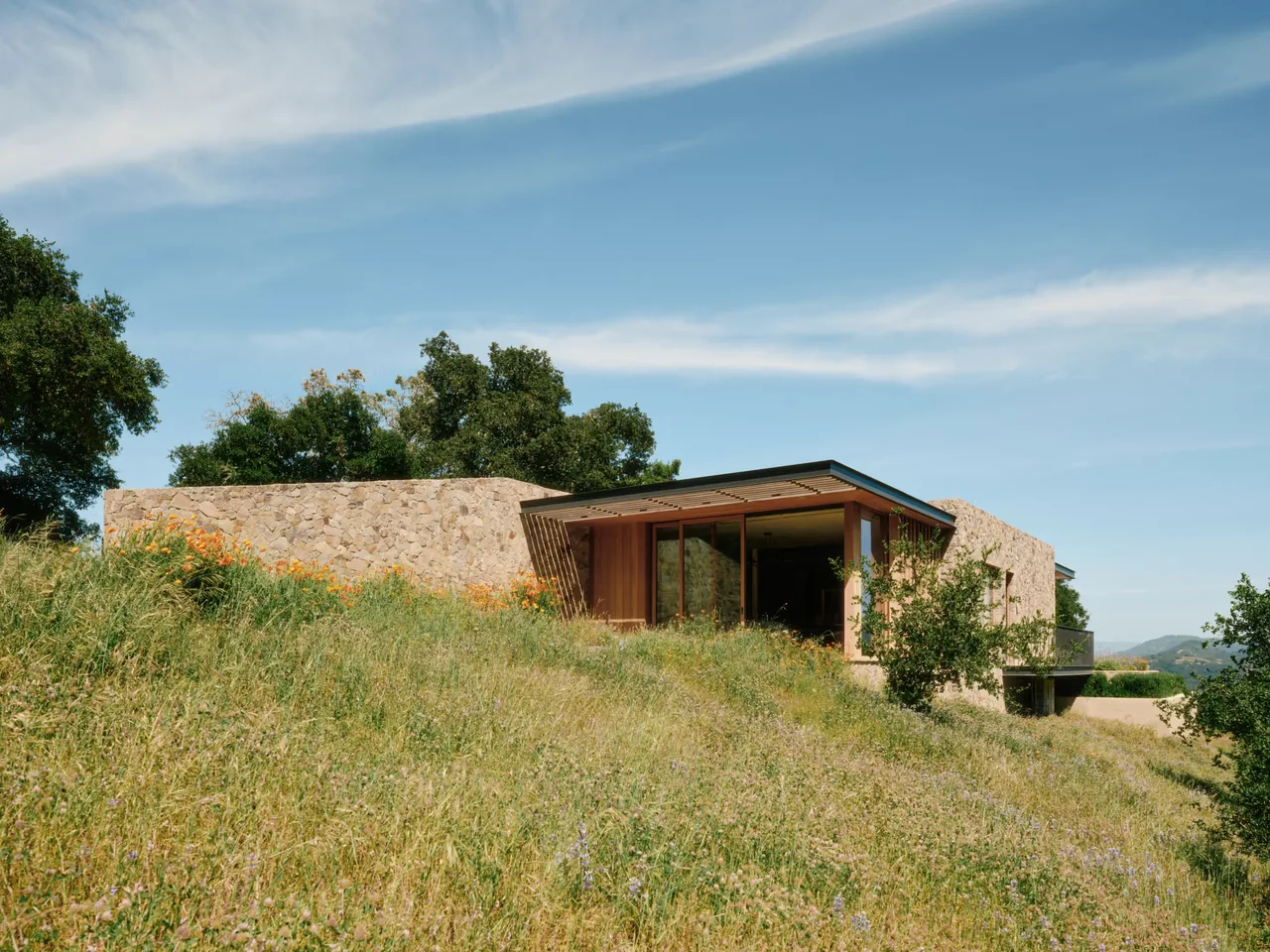 Stone Villa features natural stone walls integrated into a hillside setting with large glazing.