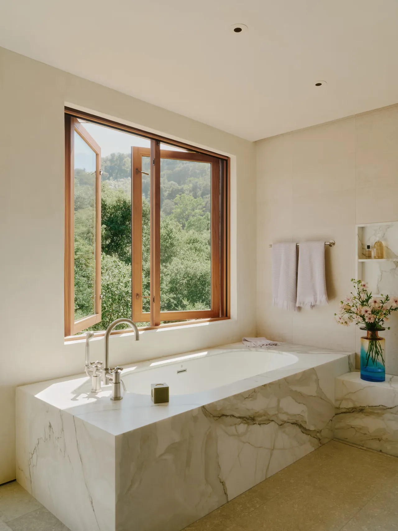 Marble tub with silver fixtures by an open wood window showcasing the natural landscape outside in Stone Villa bathroom.