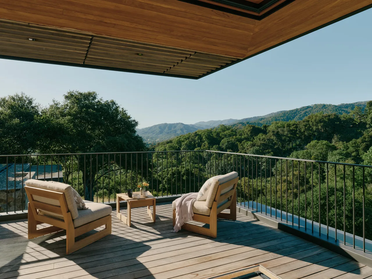 Outdoor living deck with wood lounge chairs and a small table facing a hillside view.