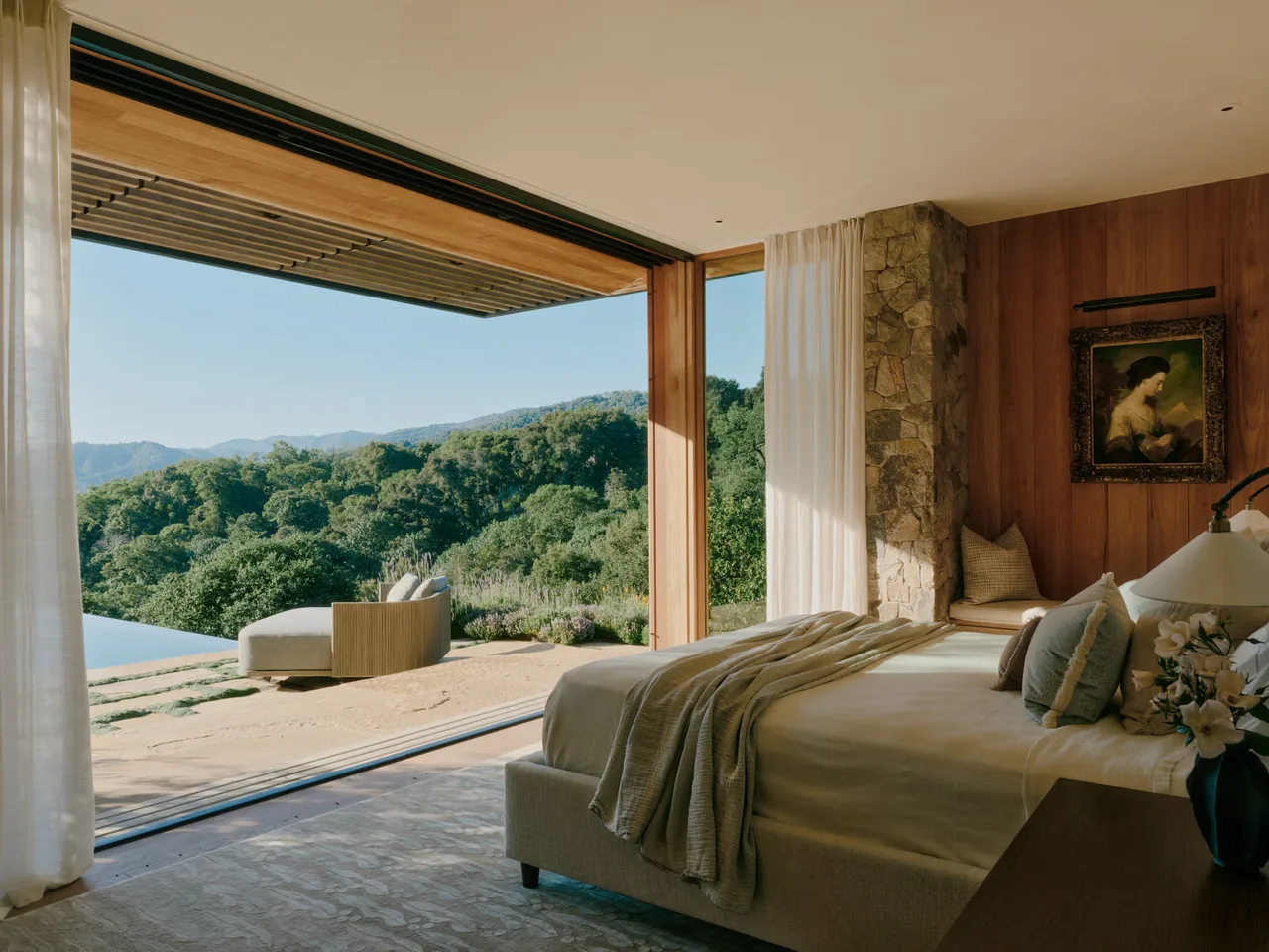 Bedroom opens with sliding glass door to lush hillside views and outdoor seating area.