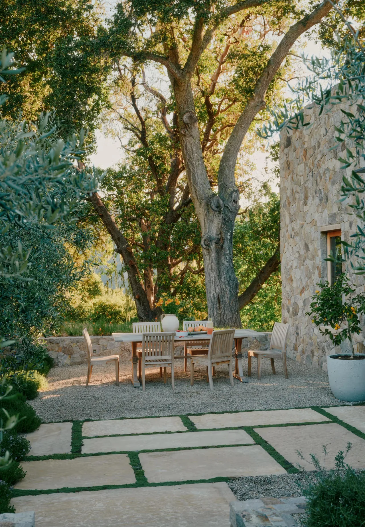 Stone Villa features an outdoor dining space with wooden furniture beside a stone exterior wall and mature trees.