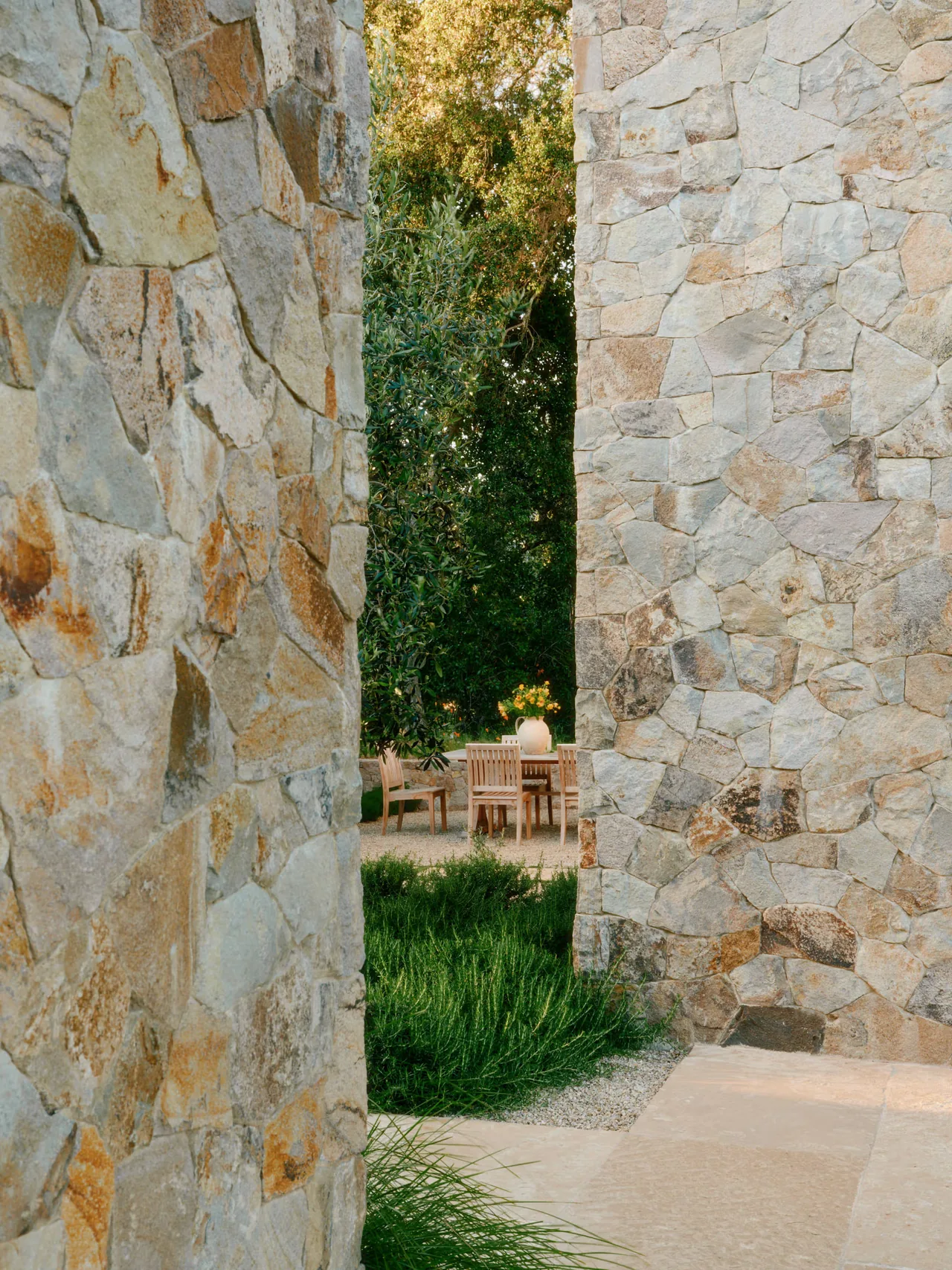 Outdoor space framed by natural stone walls with a seating area featuring wooden furniture and greenery.