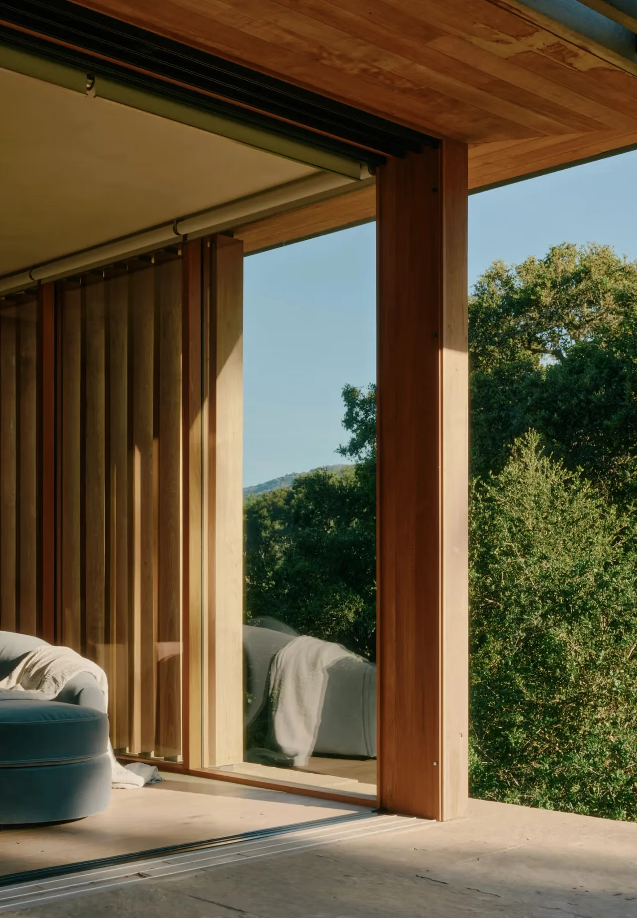 Wood-paneled room with floor-to-ceiling glass overlooking lush trees and hills beyond.