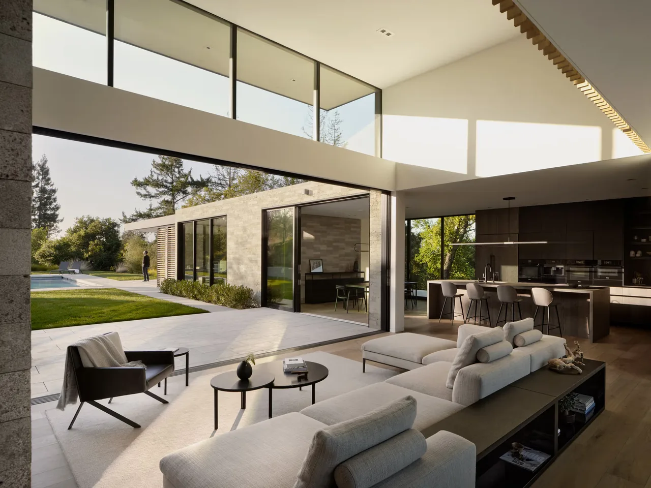 Open-concept living and kitchen area with floor-to-ceiling glazing and vaulted ceiling, connecting indoor and outdoor spaces.