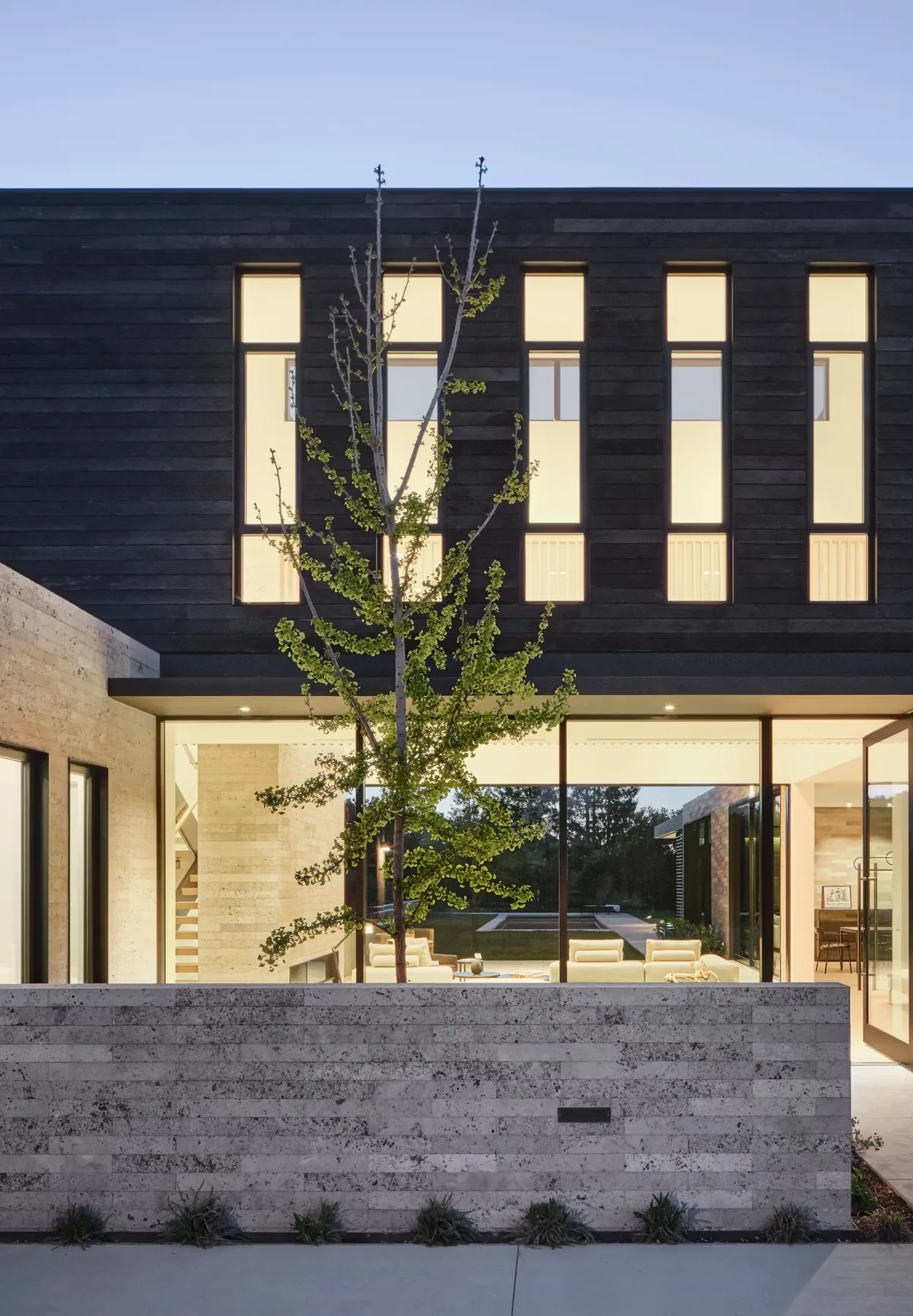 Modern two-story home facade with vertical windows and a stone wall, part of the Guzhai project in San Francisco.