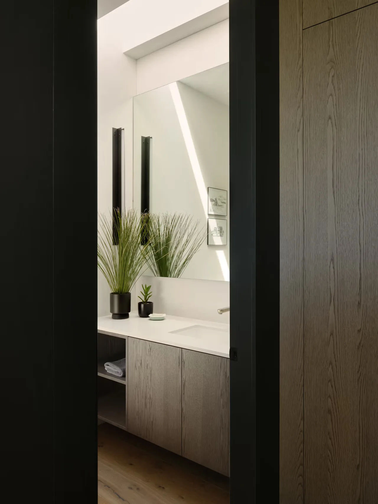 A bathroom features a wooden vanity with a white countertop and a large mirror flanked by black lights.