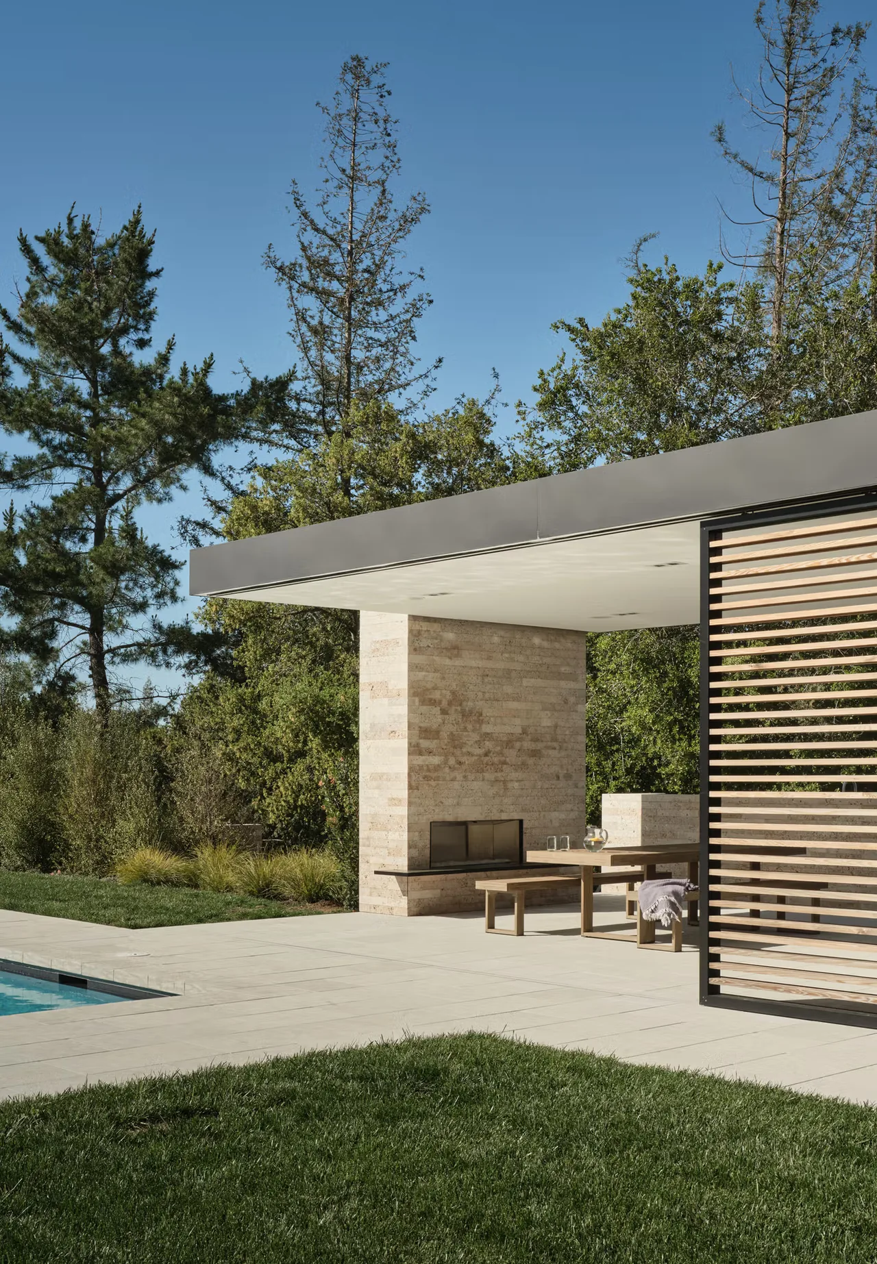 Patio at Guzhai features a travertine fireplace, wood slat screen, and wood picnic bench-style seating.