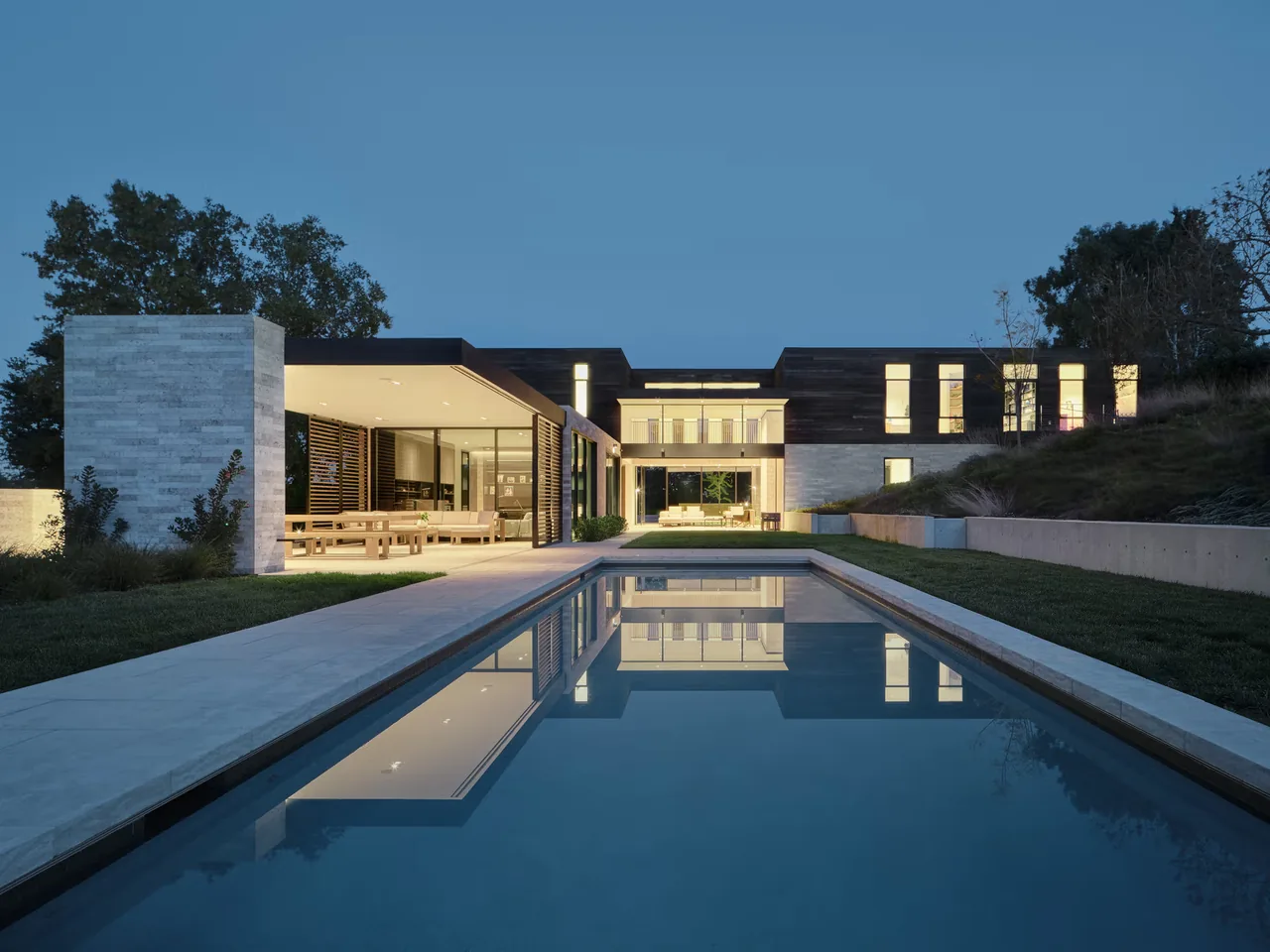 Evening view of Guzhai showing a modern home's rear exterior with pool and outdoor living space by Feldman Architecture.