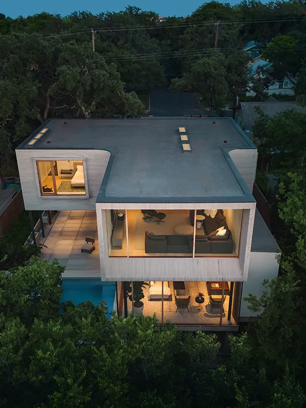 The Greenbelt Residence features a flat roof and large wood-framed windows with interior lighting visible at twilight.