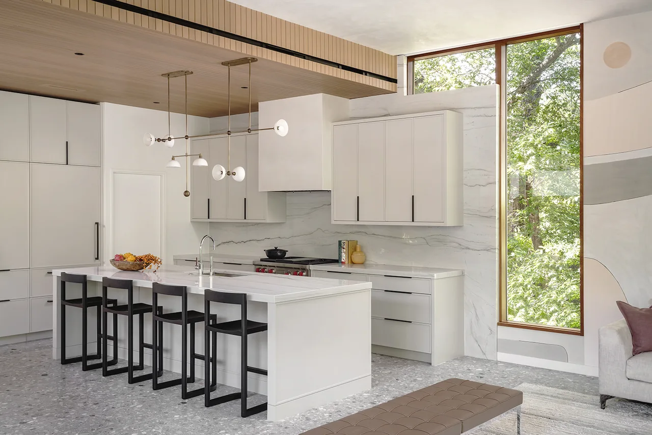 Modern kitchen features marble backsplash, wood slat ceiling, and a wall of cabinetry with integrated appliances.