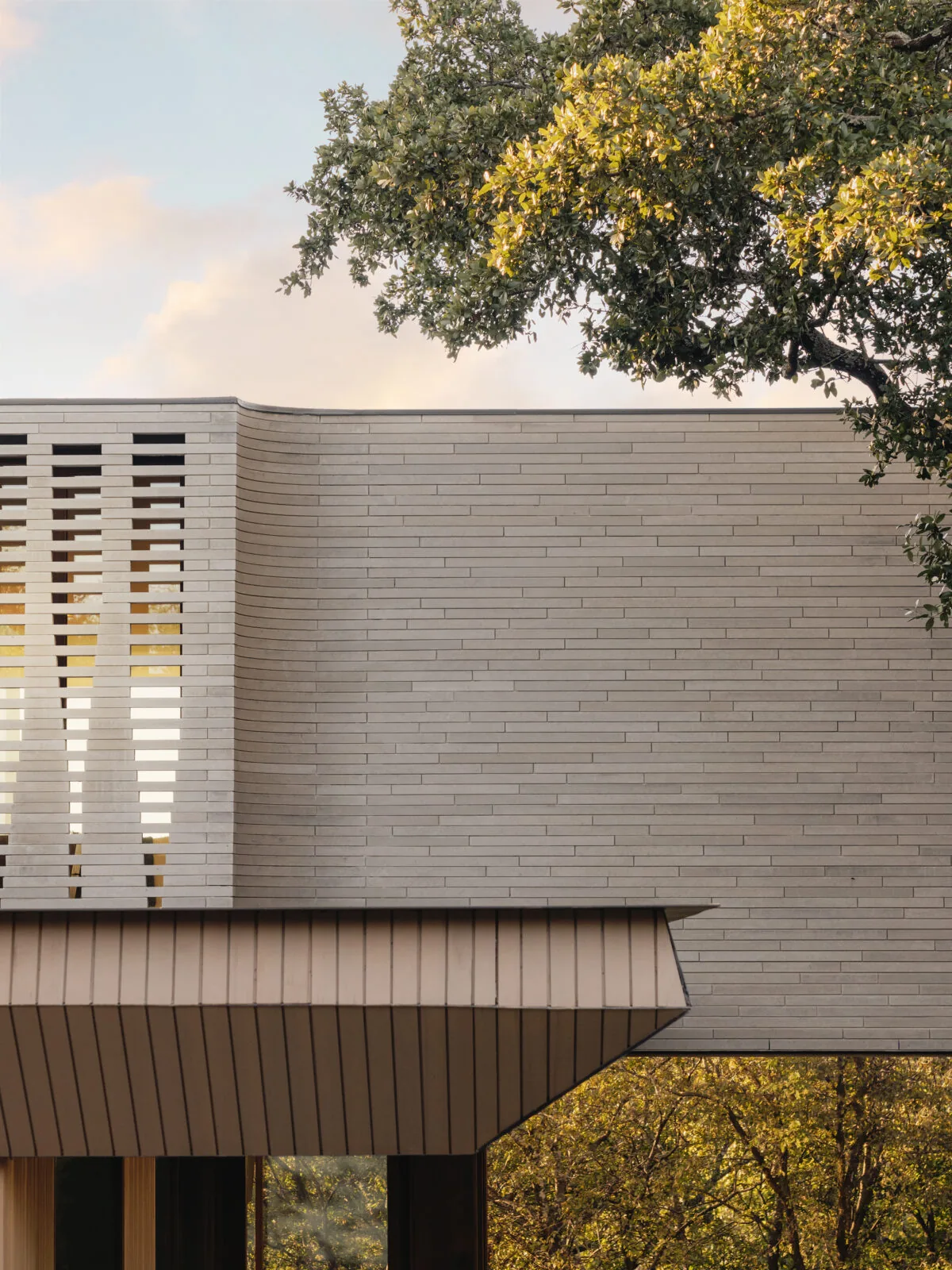 Cantilevered upper level with horizontal brick cladding and vertical wood siding below at Greenbelt Residence.
