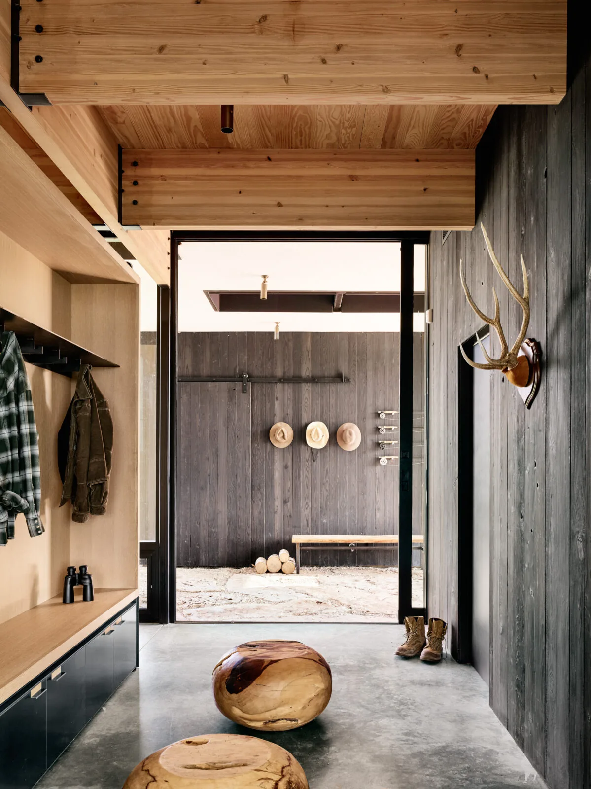 Entry hallway with blackened wood paneling, natural wood ceiling, and concrete floor at Llano Retreat by Hsu Office of Architecture.
