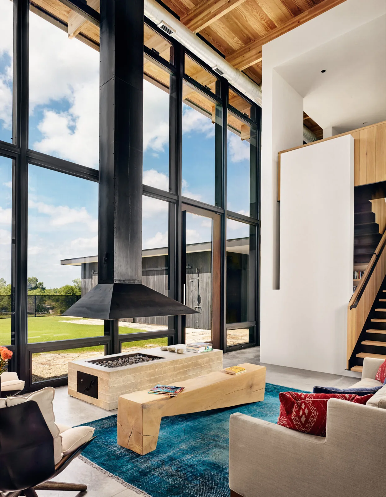 Living room with floor-to-ceiling black-framed windows and a suspended black metal fireplace over a stone hearth.