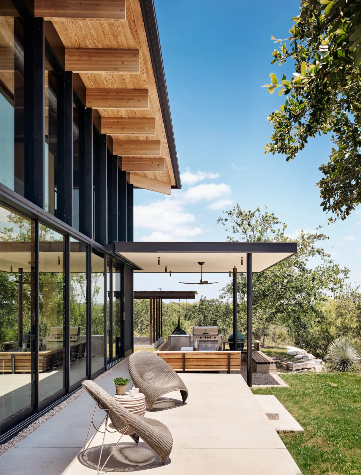 Llano Retreat patio with wood ceiling beams, floor-to-ceiling glazing, and outdoor grill by Hsu Office of Architecture.