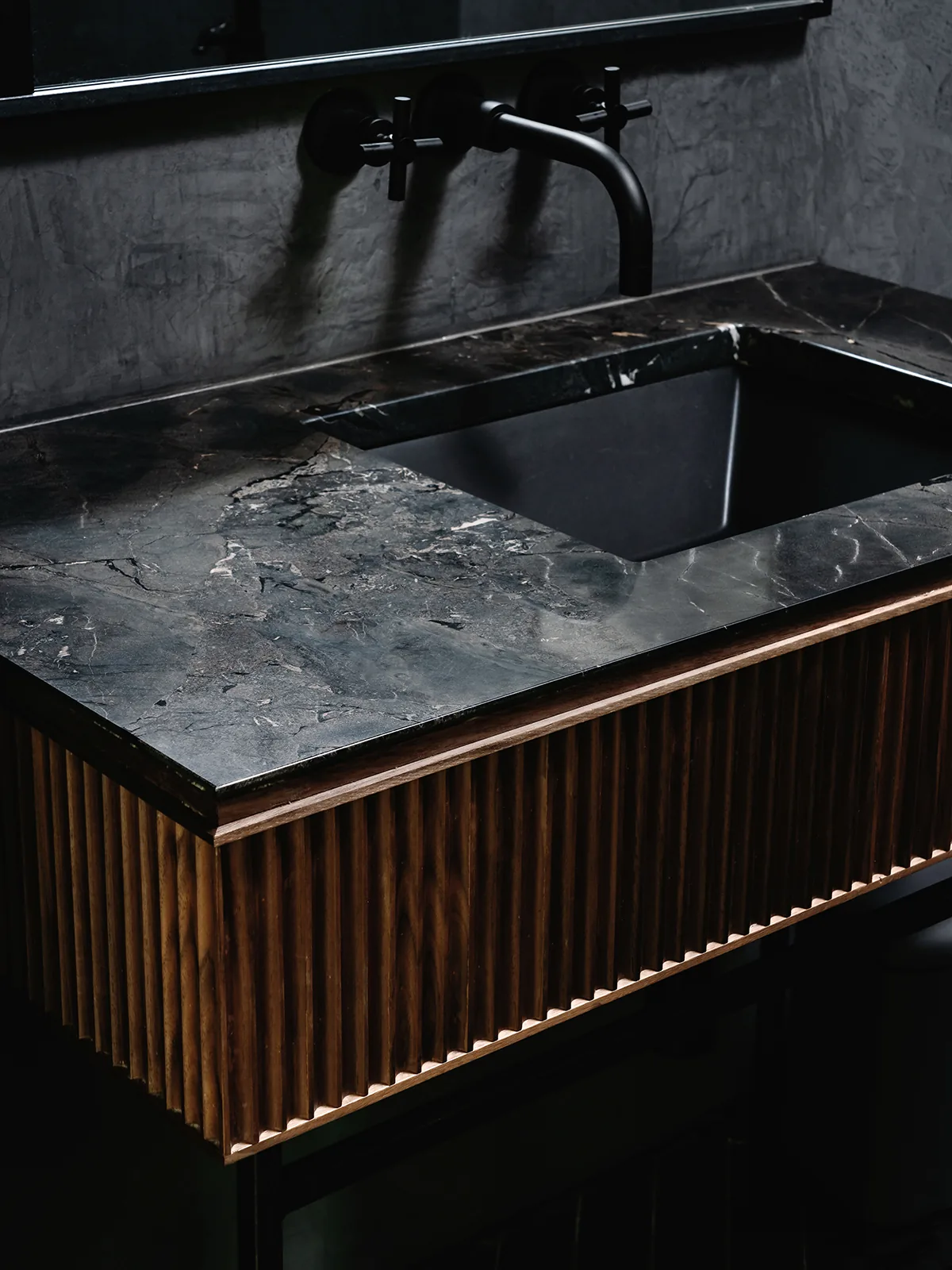Detail of kitchen area with textured stone countertop, black sink, and ribbed wood cabinetry at Rollingwood Residence.