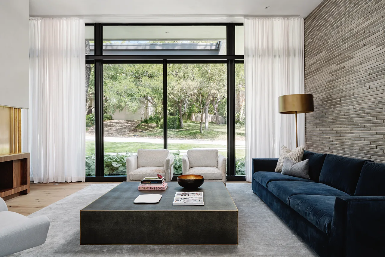 Living room with floor-to-ceiling black window frames and a textured linear stone feature wall in Rollingwood Residence by Hsu Office of Architecture.