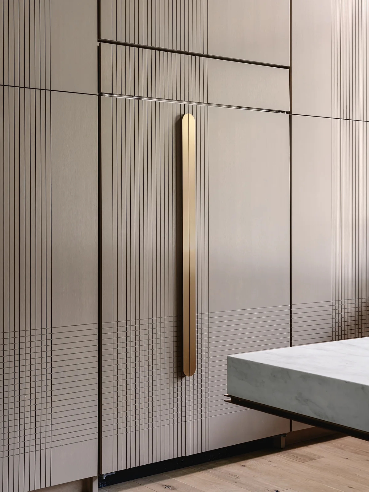 Kitchen cabinetry features fine linear etched patterns with a long brass vertical pull handle and marble countertop edge visible.