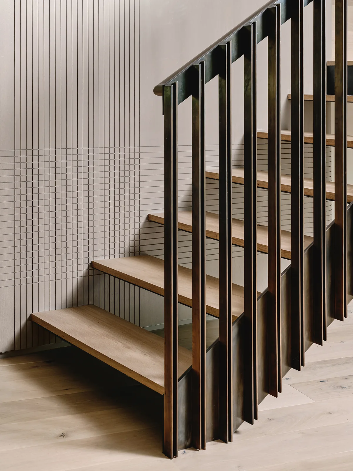 Interior view of a staircase featuring wood treads and vertical blackened steel balusters with etched line wall detailing.