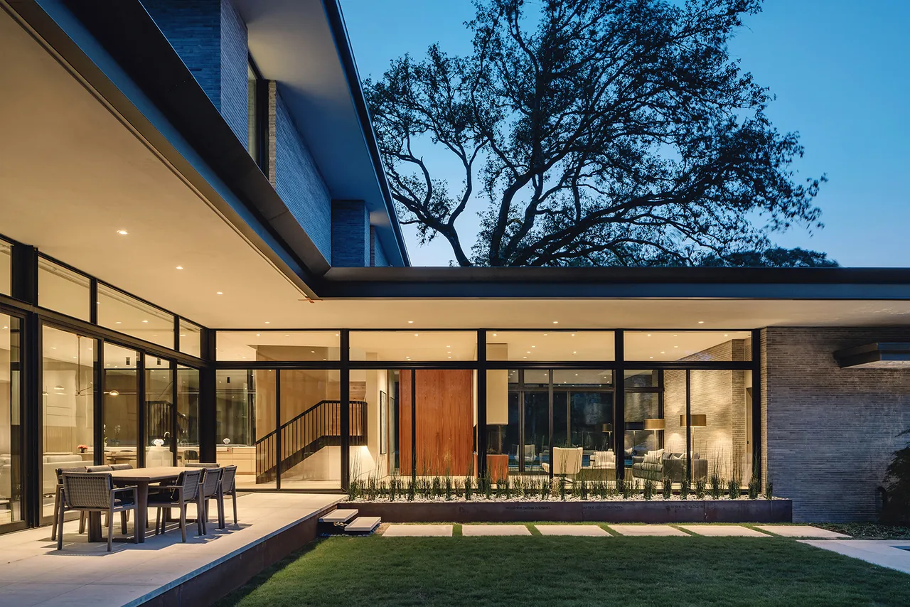 Rollingwood Residence shows a two-story modern design with floor-to-ceiling glazing and wide eaves over a landscaped lawn patio.