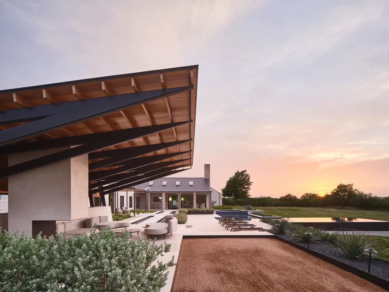 Hilltop Ranch features a cantilevered roof over an outdoor living space adjacent to a pool and landscaped grounds at sunset.