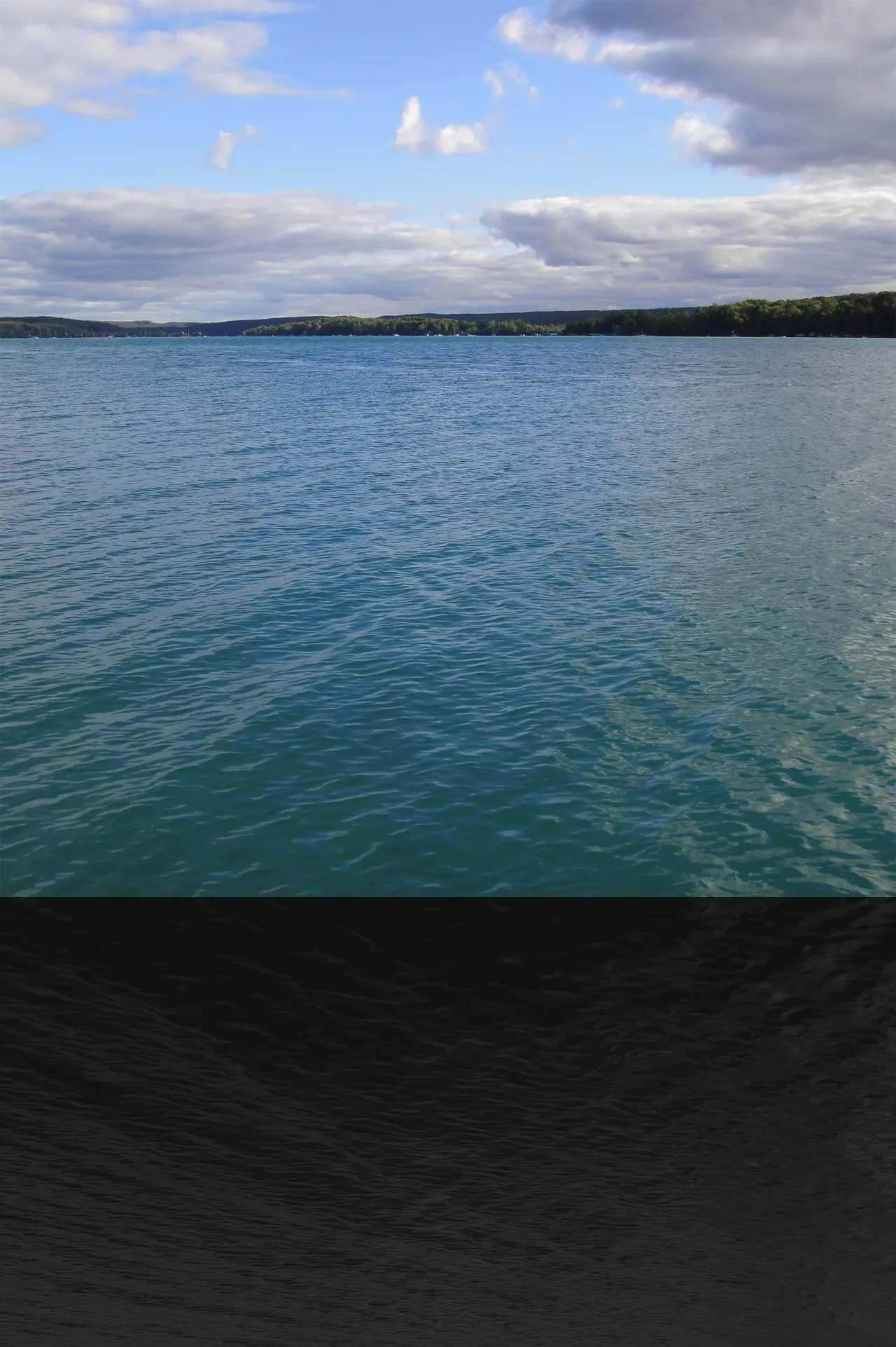 Walloon Lake showing water and distant wooded shore under partly cloudy sky.