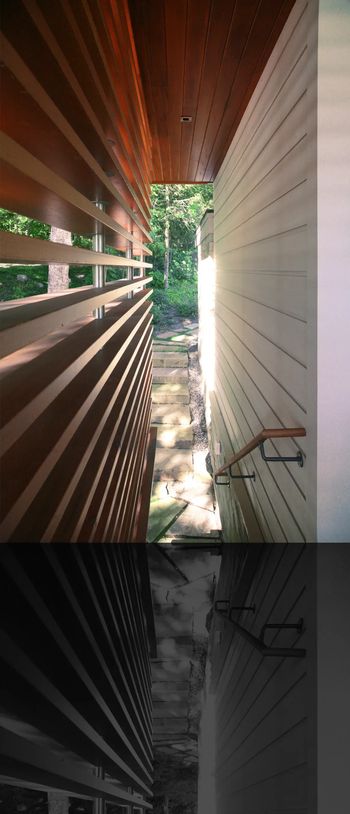 Narrow outdoor passageway with wood slatted wall and white siding featuring stone paving steps and a handrail.