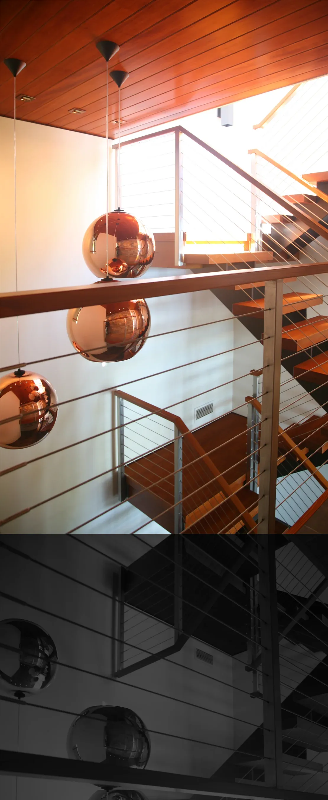 Modern stairwell featuring cable metal railings and reflective copper globe pendant lights beneath a wooden ceiling.