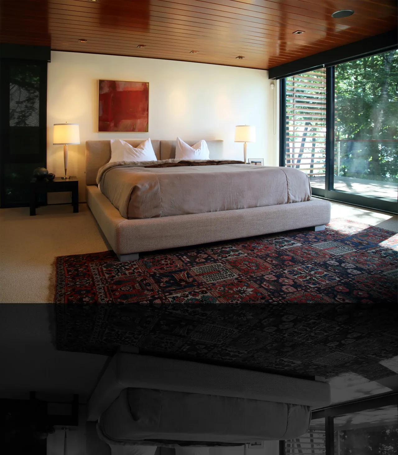This bedroom features a plush bed with a textured area rug and large sliding glass doors providing a view of trees outside.