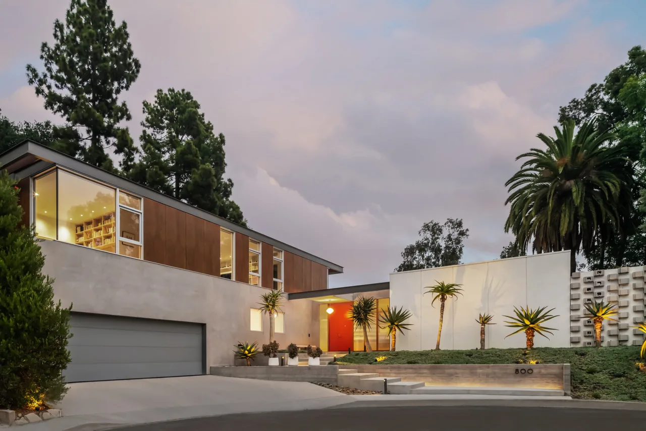 Modern two-story house exterior at dusk with large windows and landscaped front yard.