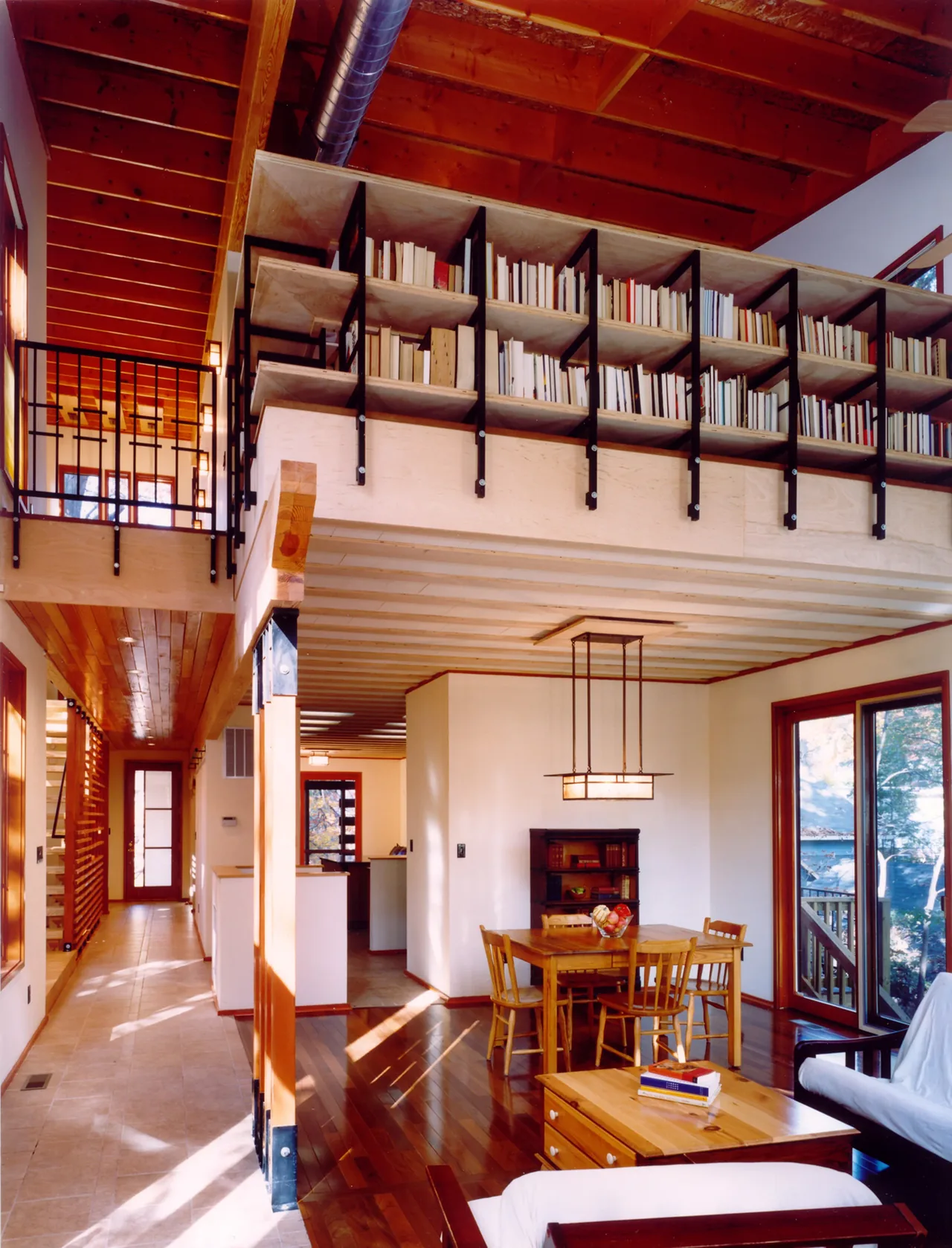 Perch House dining area and living room with wood ceiling beams and an upper-level bookshelf balcony.