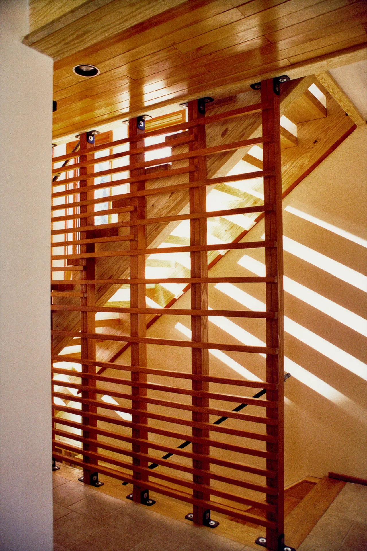 The Perch House stairway features a wood slat railing and ceiling beams casting light patterns.