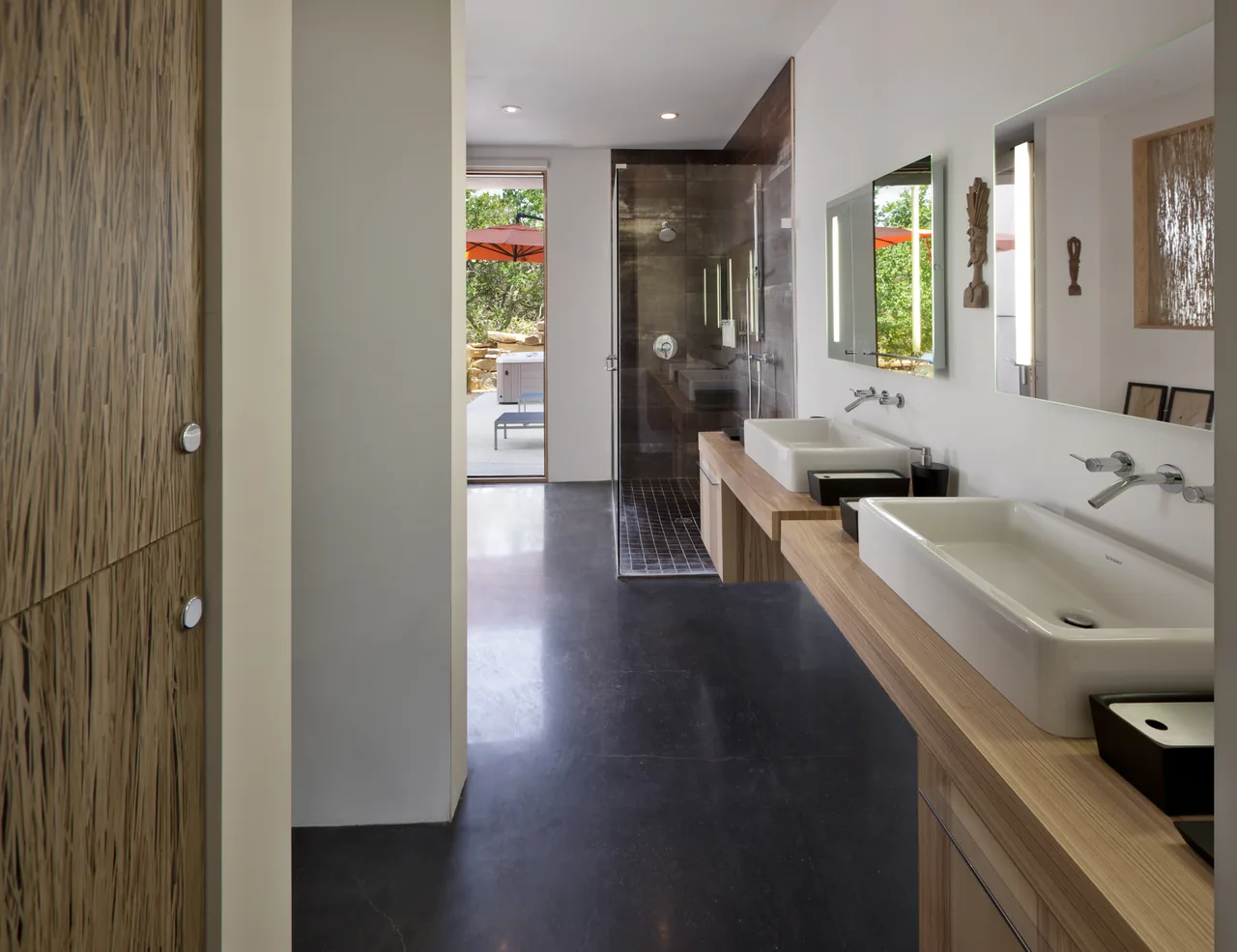 Bathroom in Oblio House featuring dual vessel sinks and a glass-enclosed shower with dark tile walls.