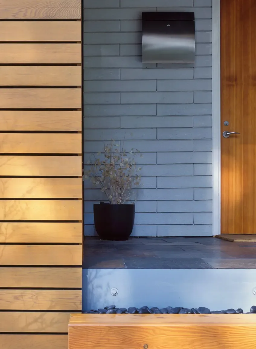 Entry area of the Cavehill project features horizontal wood siding, a wooden door, and a stone tile porch with a planter.