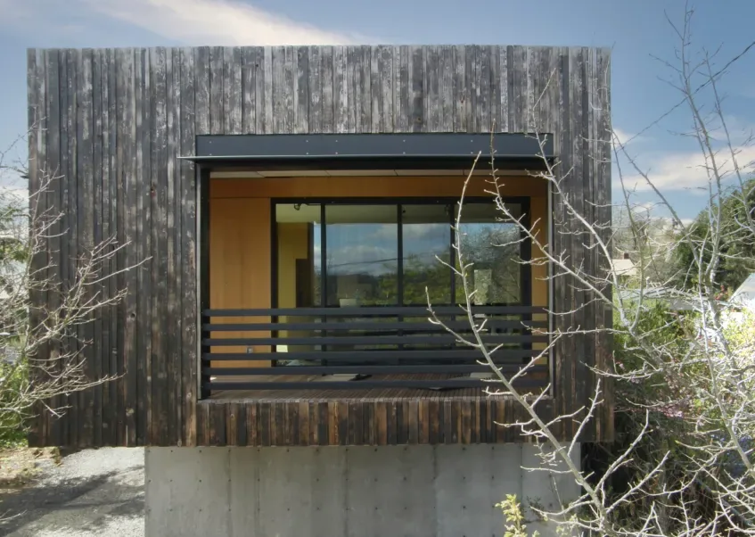 The house features vertical charred wood siding with a recessed balcony and large glass window framed in black metal.