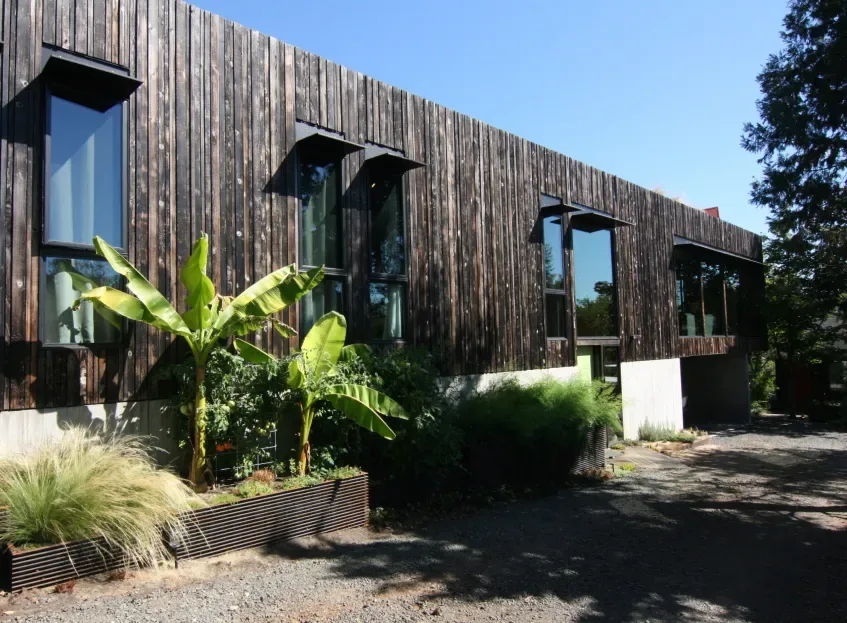 House exterior clad in weathered vertical wood siding with black metal awnings over tall windows.