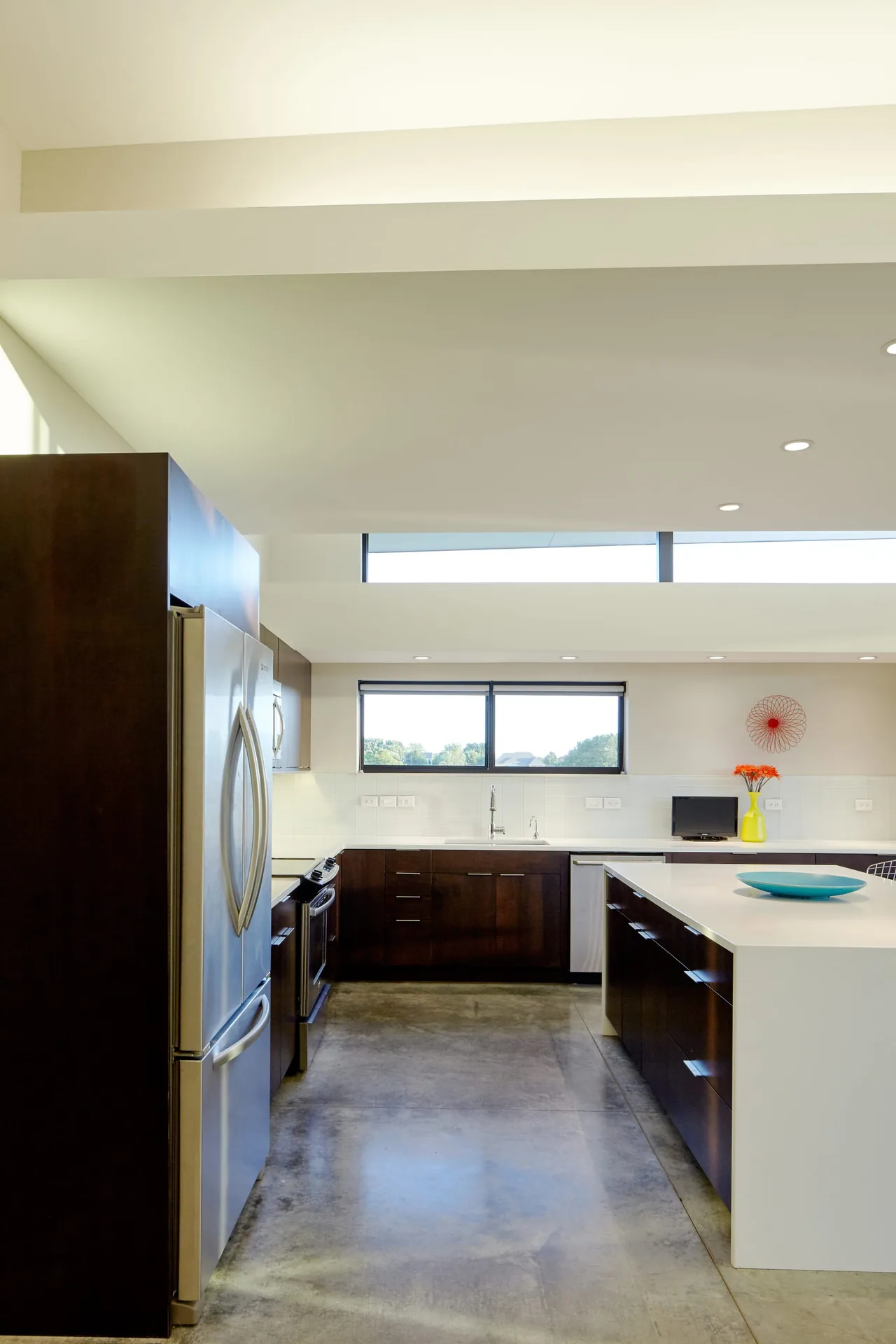 Modern kitchen features dark cabinetry, a large white island, stainless steel appliances, and clerestory windows for natural light.