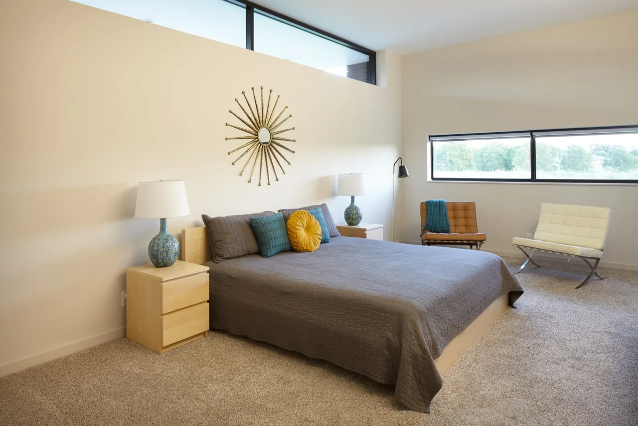 The bedroom in Byers Residence features high clerestory windows and a gray bedspread with vibrant accent pillows.