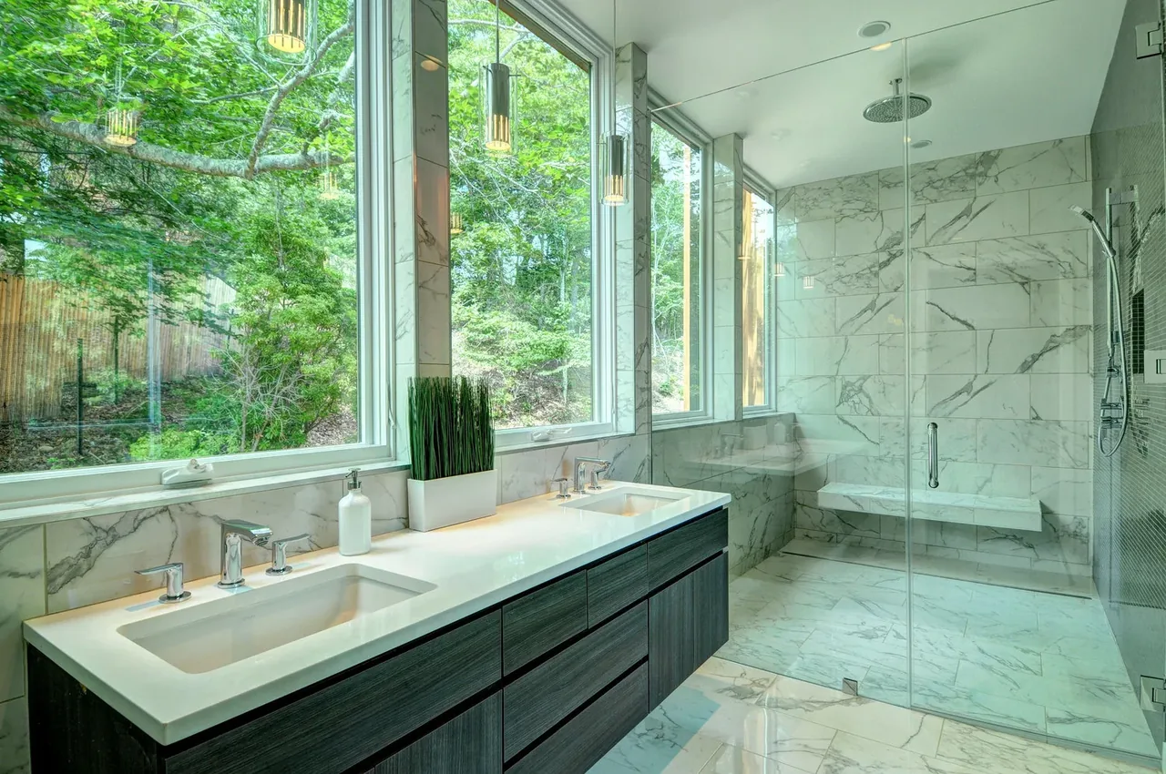 Bright bathroom features two sinks, marble tile surfaces, and a spacious walk-in shower with bench seating.