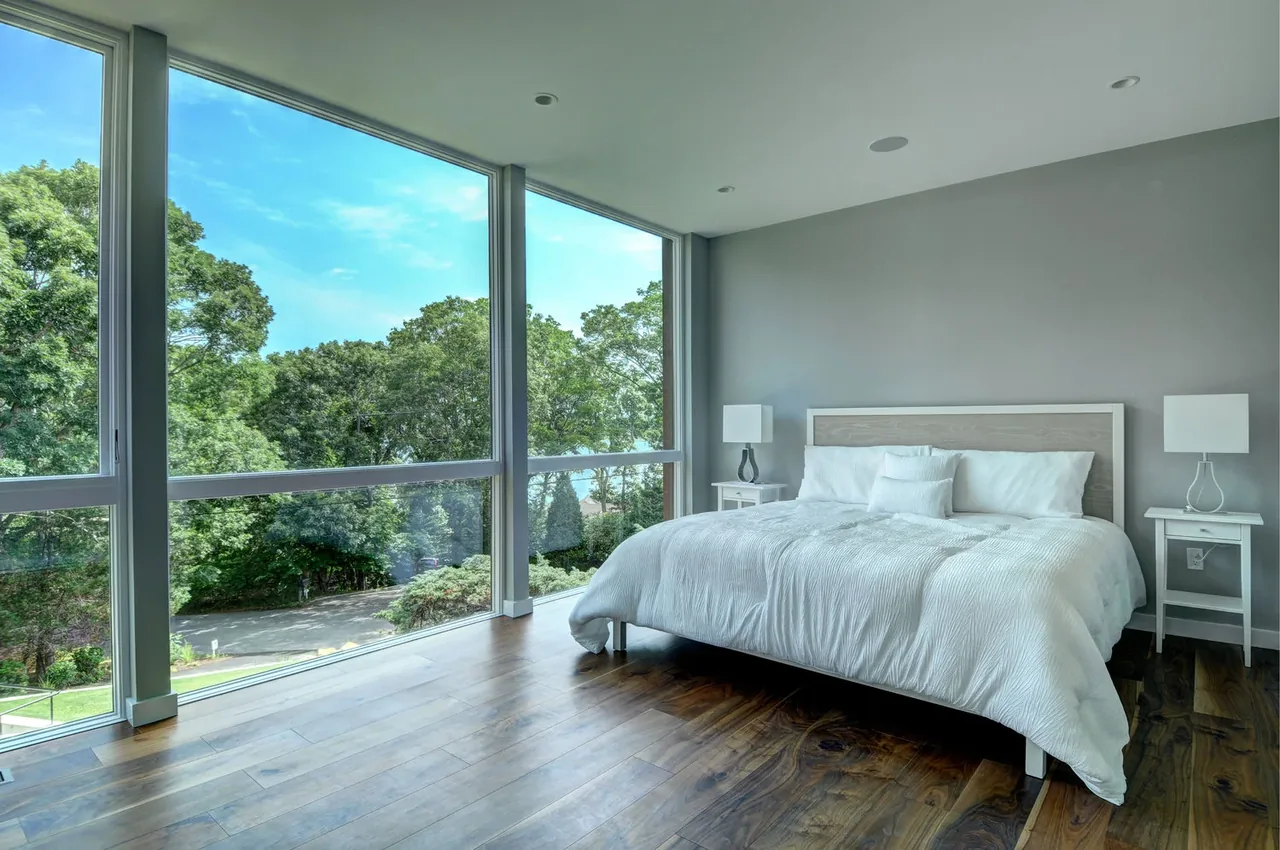 Bright bedroom featuring floor-to-ceiling windows with green landscape views and contemporary wood flooring.