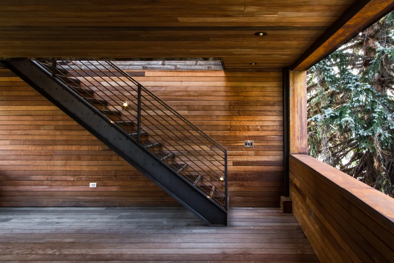 Wood-clad exterior porch with metal stairs and railing overlooking forested landscape.