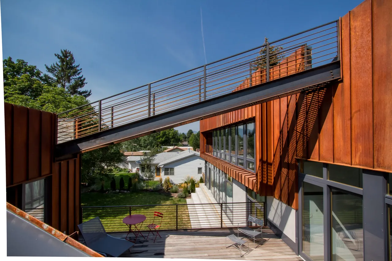 Rust-colored metal facade and large row of windows viewed from a deck with metal railings at the Wren Residence.
