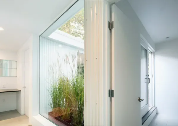 Interior view of a modern minimalist room featuring a large picture window and glass door opening to an outdoor planted area.