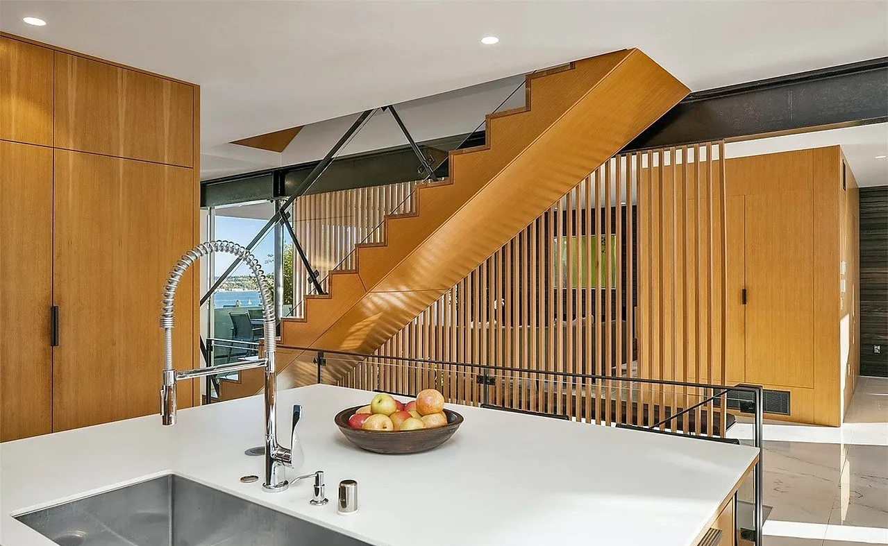 Modern kitchen island with white countertop and built-in sink, adjacent to a wooden slatted staircase and cabinetry.